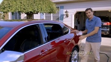 A man is standing next to a red car in a garage.