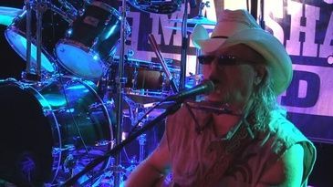 A man in a cowboy hat is singing into a microphone on a stage.