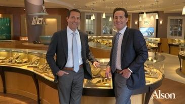 Two men in suits and ties are standing next to each other in a jewelry store.