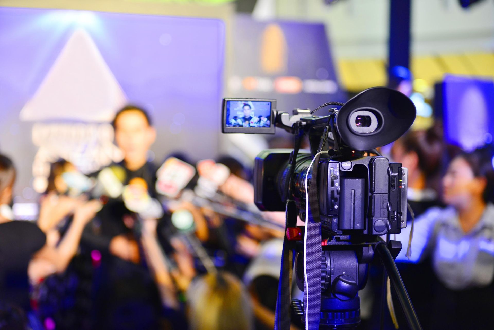 A video camera is sitting on a tripod in front of a crowd of people.