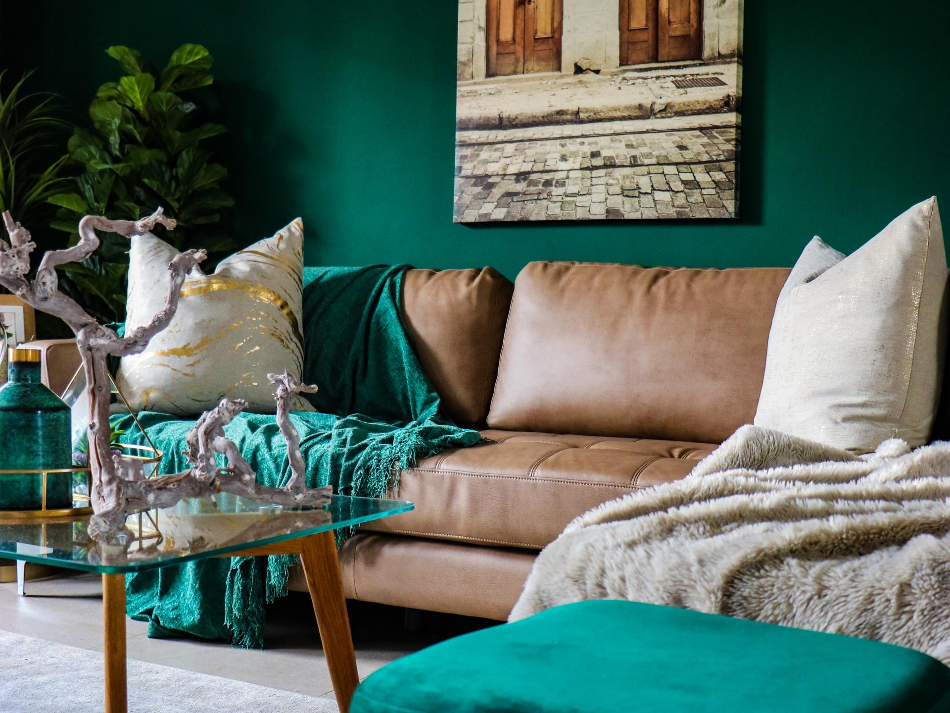 A living room with green walls , a brown couch , a coffee table , and a painting on the wall.