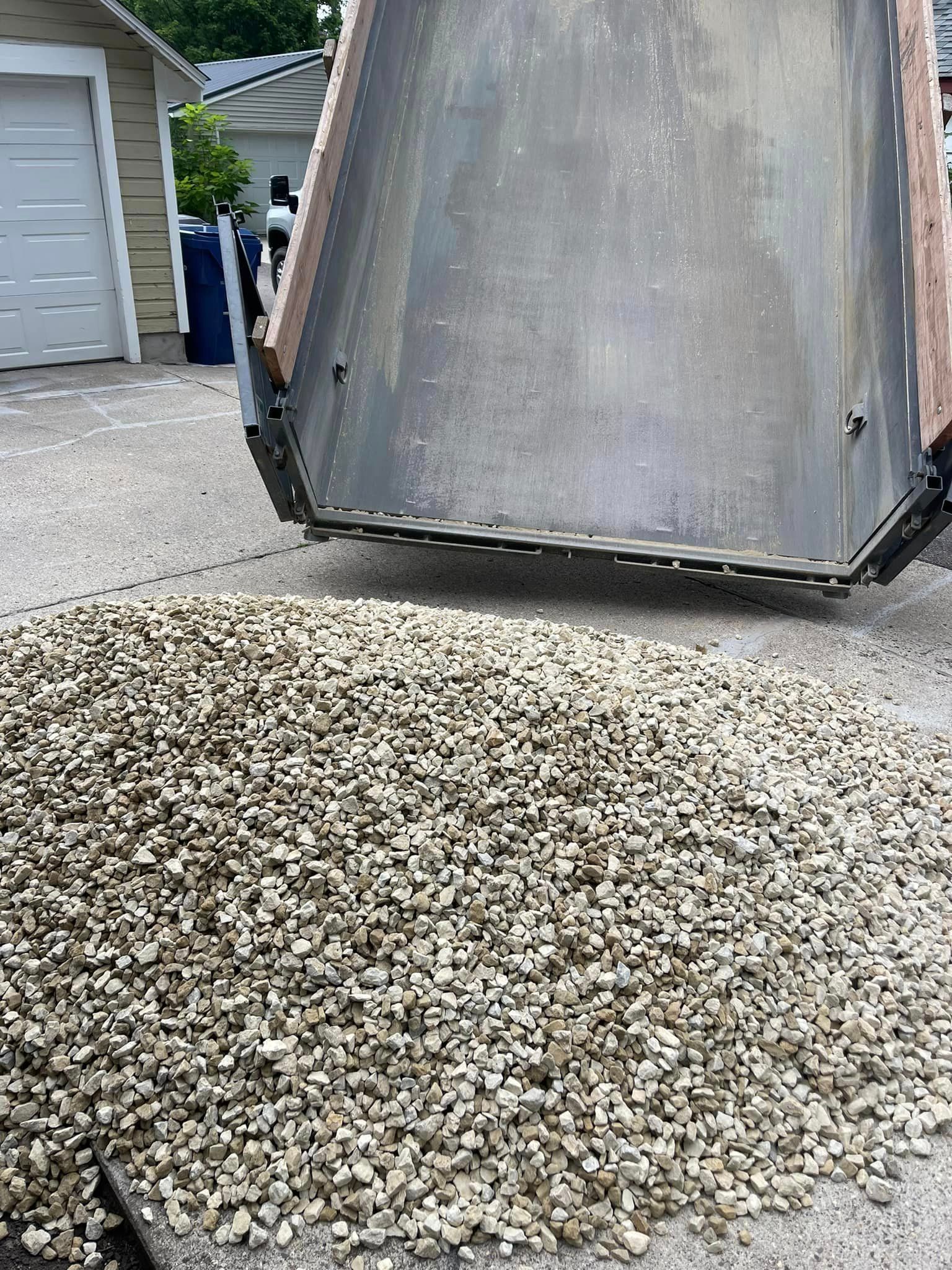 A dump truck is being loaded with gravel in a driveway.