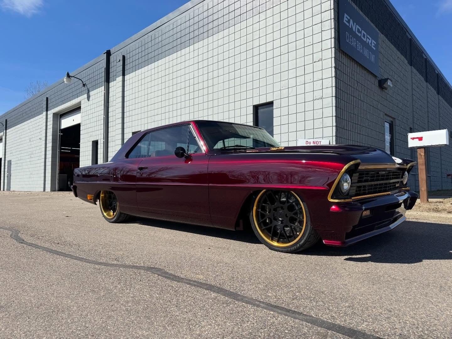 Maroon lowered classic car parked outside a warehouse under a blue sky