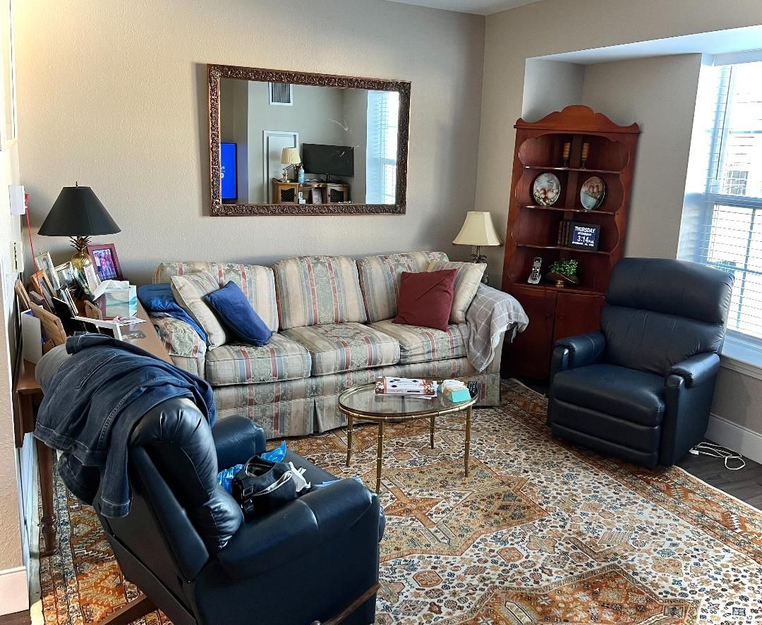 Cozy living room with sofa, recliner, corner cabinet, and rug. A large mirror reflects a room.