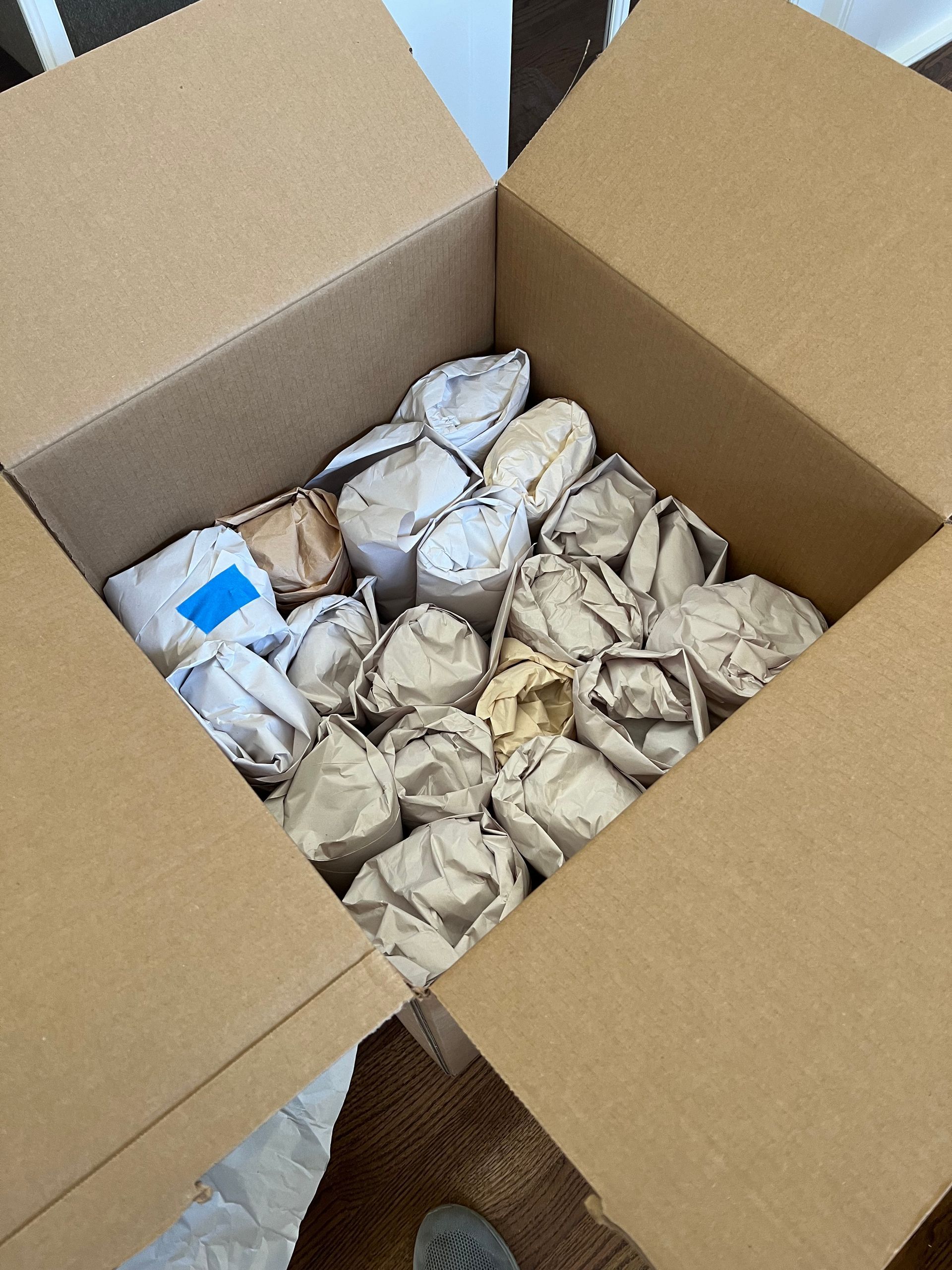 Open cardboard box filled with wrapped items, likely for shipping, protected by crumpled paper.