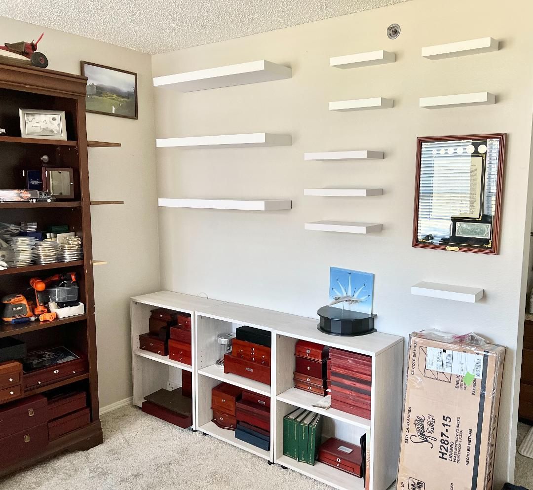Room with bookshelves and floating white shelves on a tan wall. Books and objects are on the shelves.