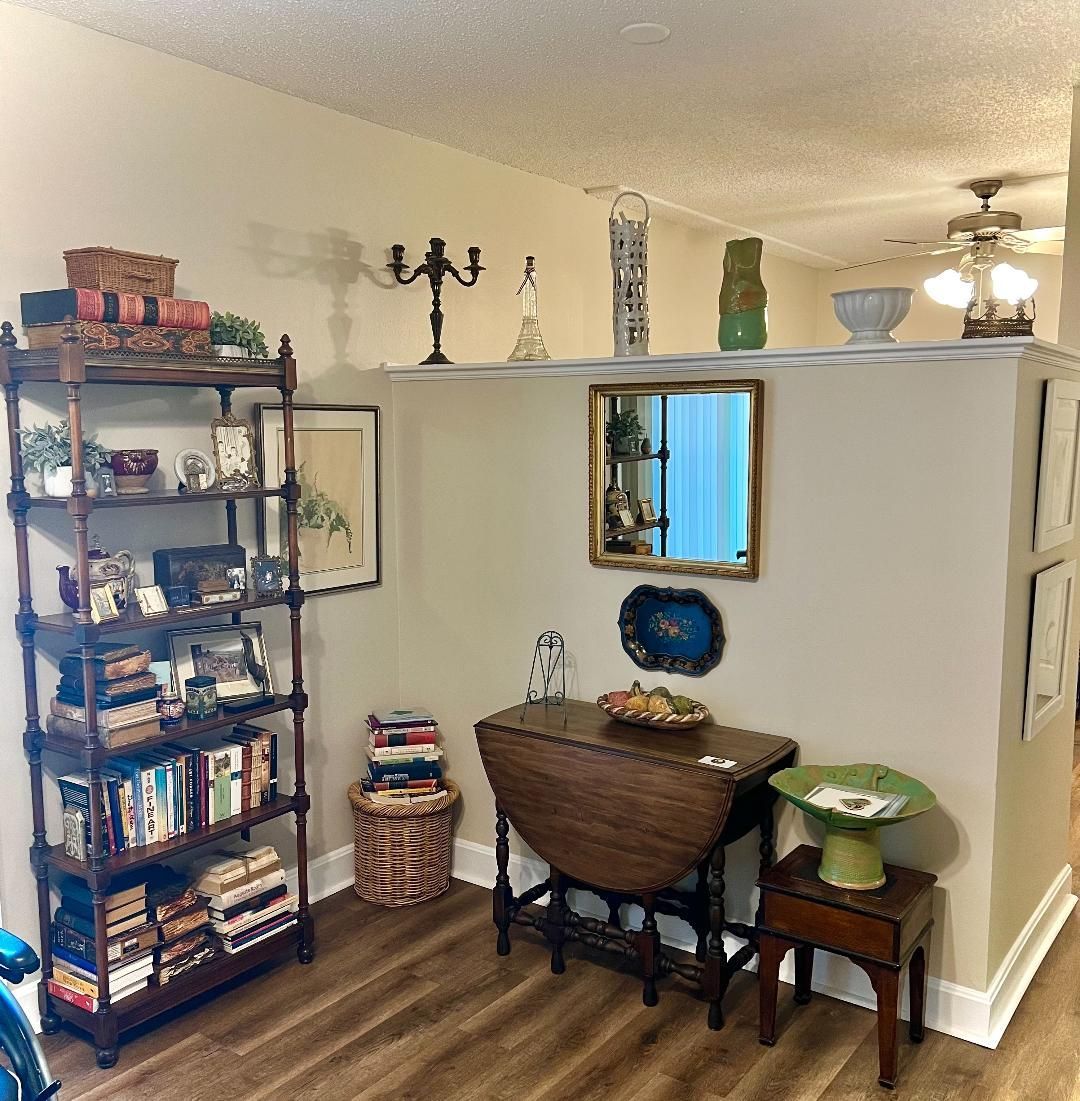 A room with a bookshelf, table, and decorative items. Light-colored walls and dark furniture.