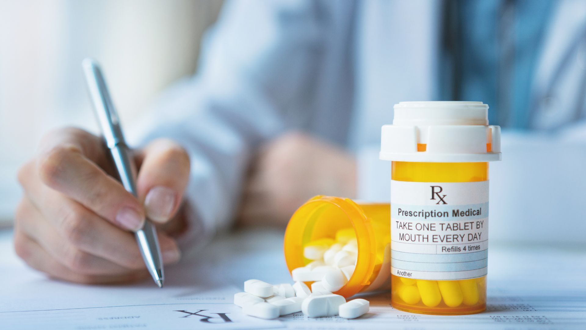 A person is writing a prescription next to a bottle of pills.