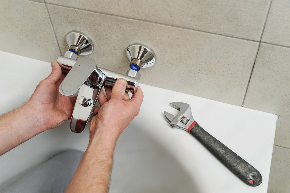 a man is fixing a bathtub faucet with a wrench .