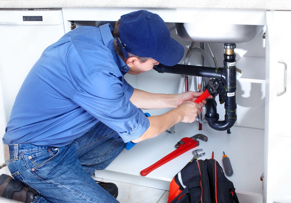 A young female plumber sitting on the floor expertly repairing a bathroom sink.