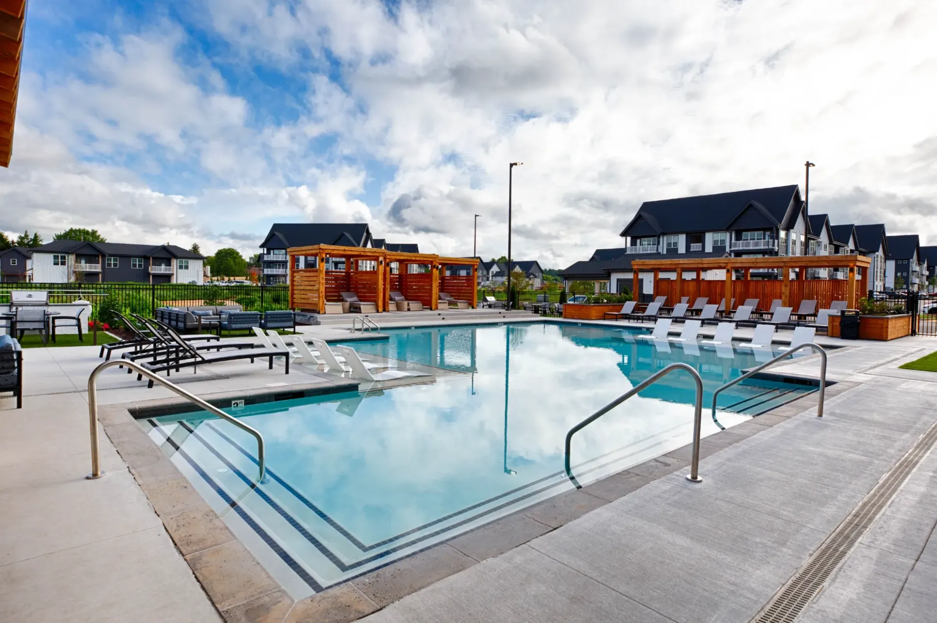 Outdoor community swimming pool with loungers, shaded cabanas, and surrounding apartment buildings.
