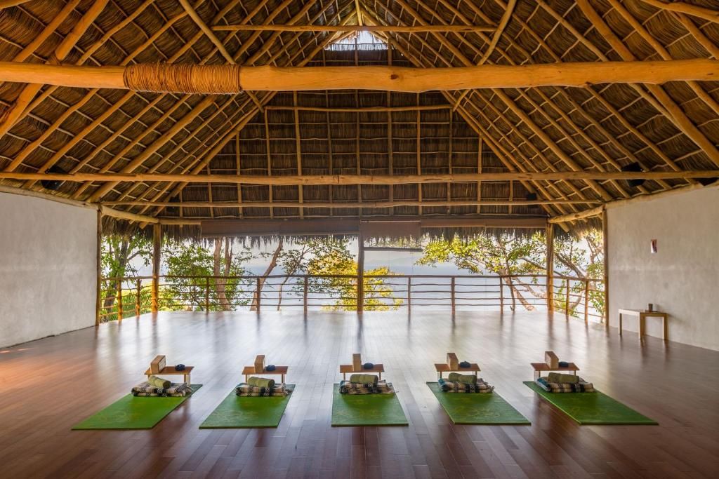 Open-air yoga pavilion with six mats facing a tropical view through wooden rafters.