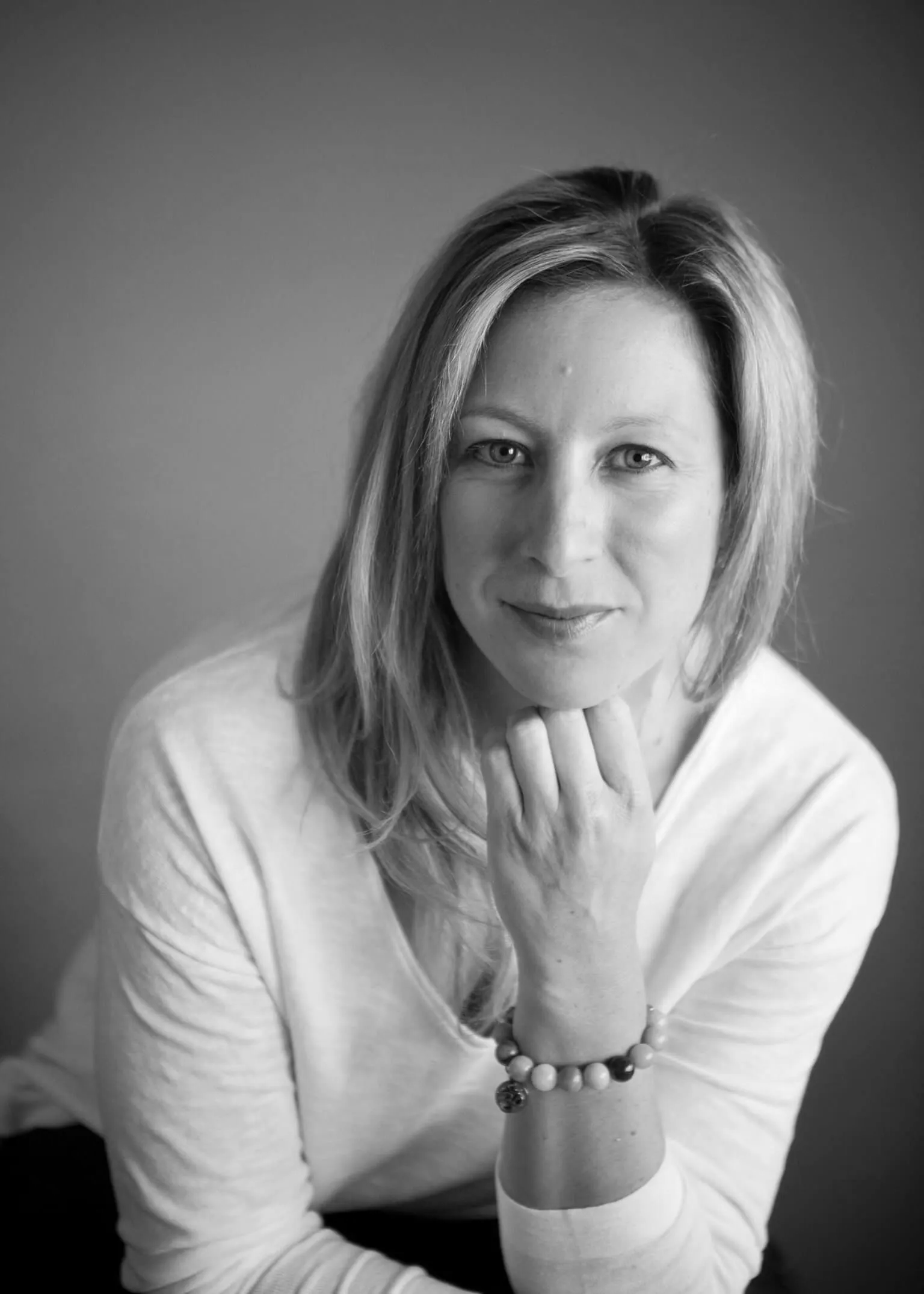 Black-and-white portrait of a person resting their chin on their hand, looking at the camera.