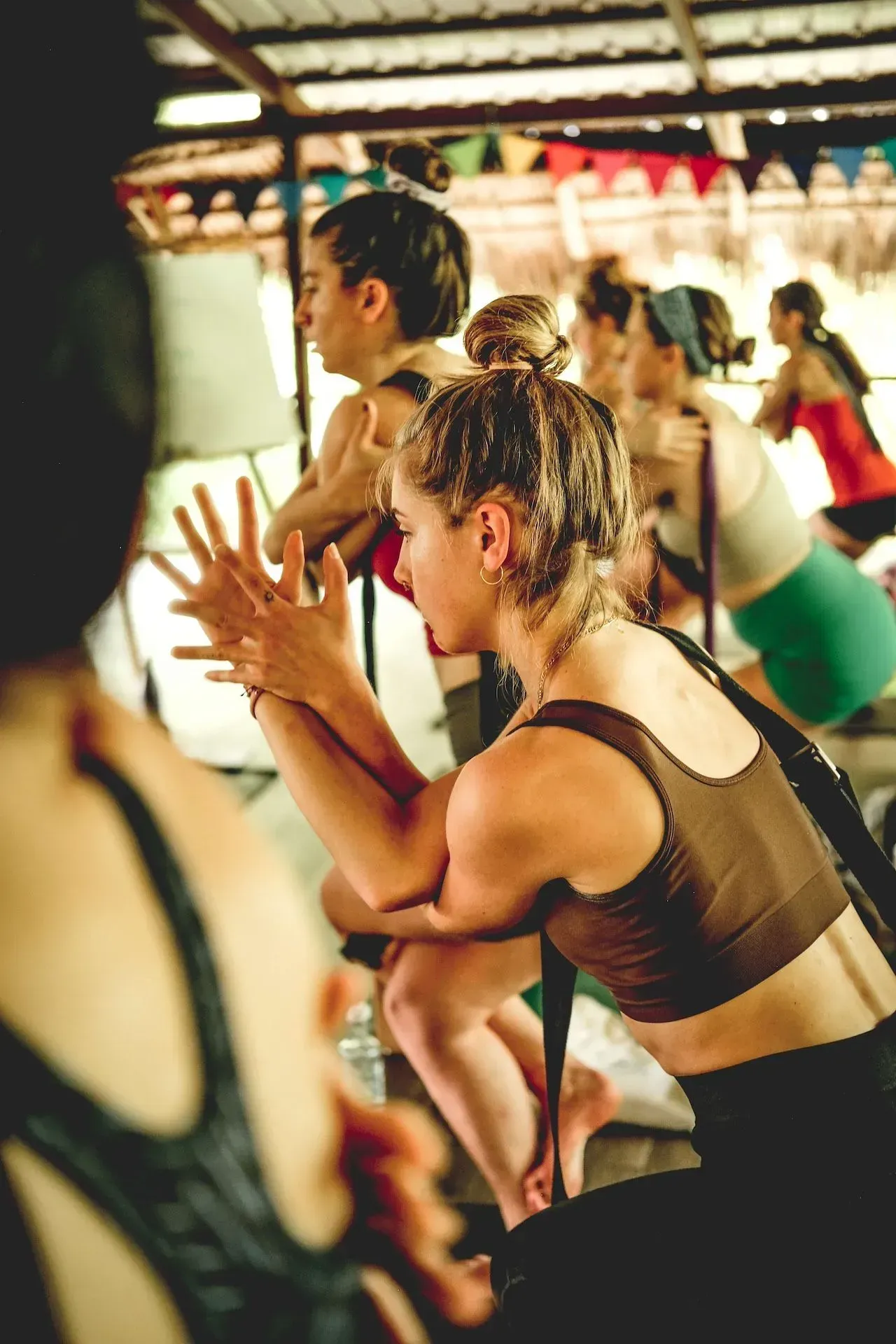 People practicing yoga in a studio, with a woman in a brown top in the foreground.