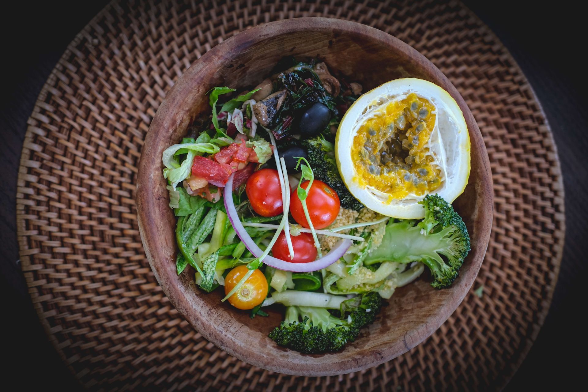 A wooden bowl filled with vegetables and a lemon on a table.
