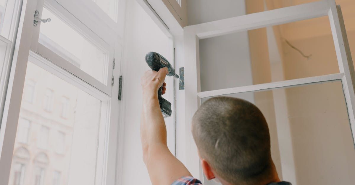 A man is using a drill to fix a window.