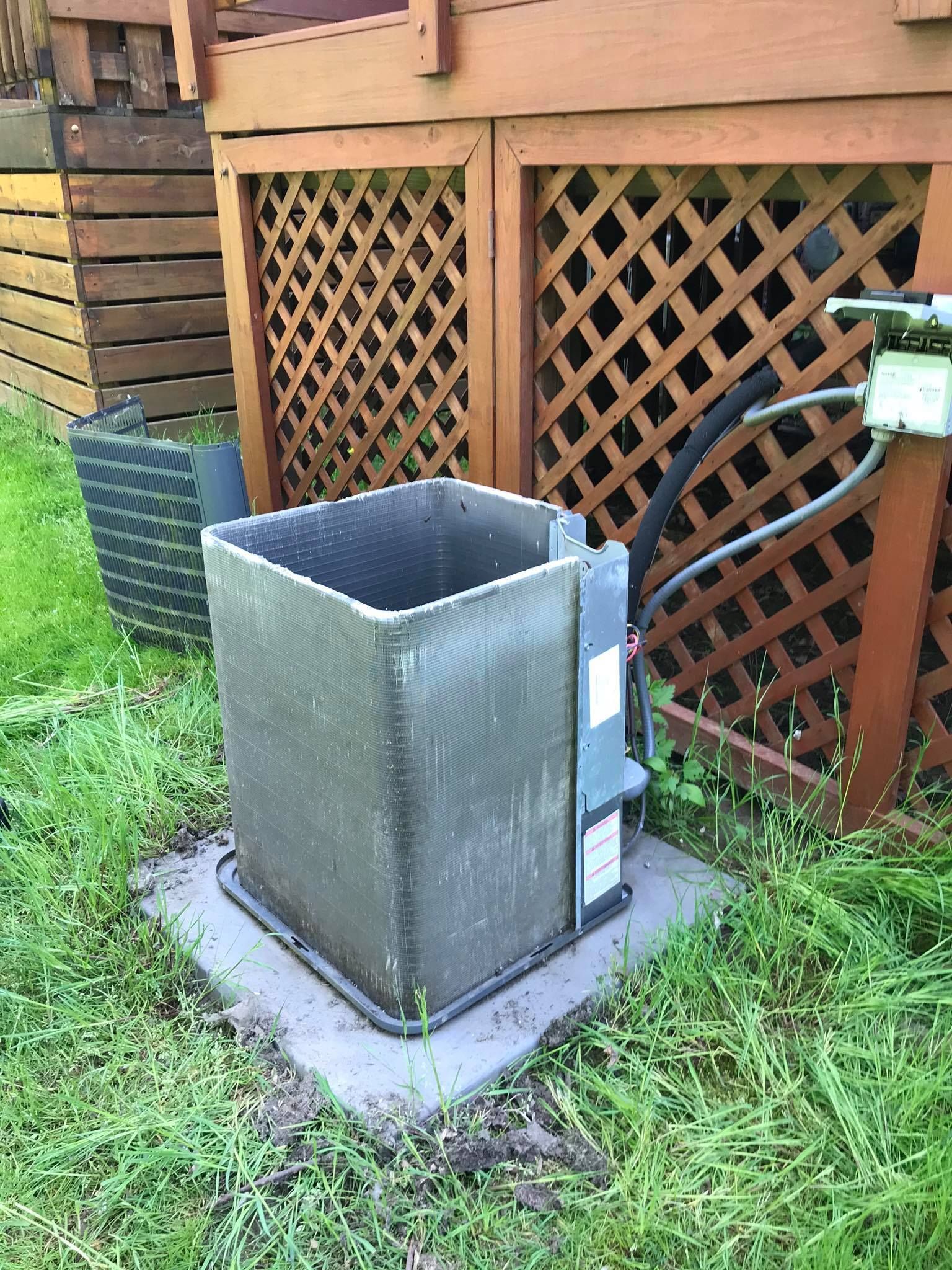 An air conditioner is sitting in the grass next to a wooden fence.