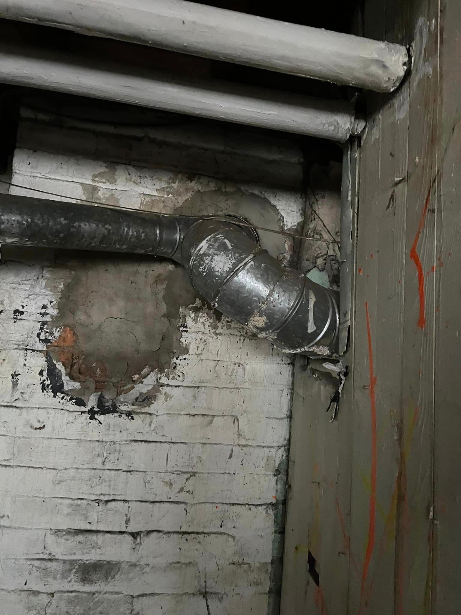 A pipe is hanging from a brick wall in a basement.