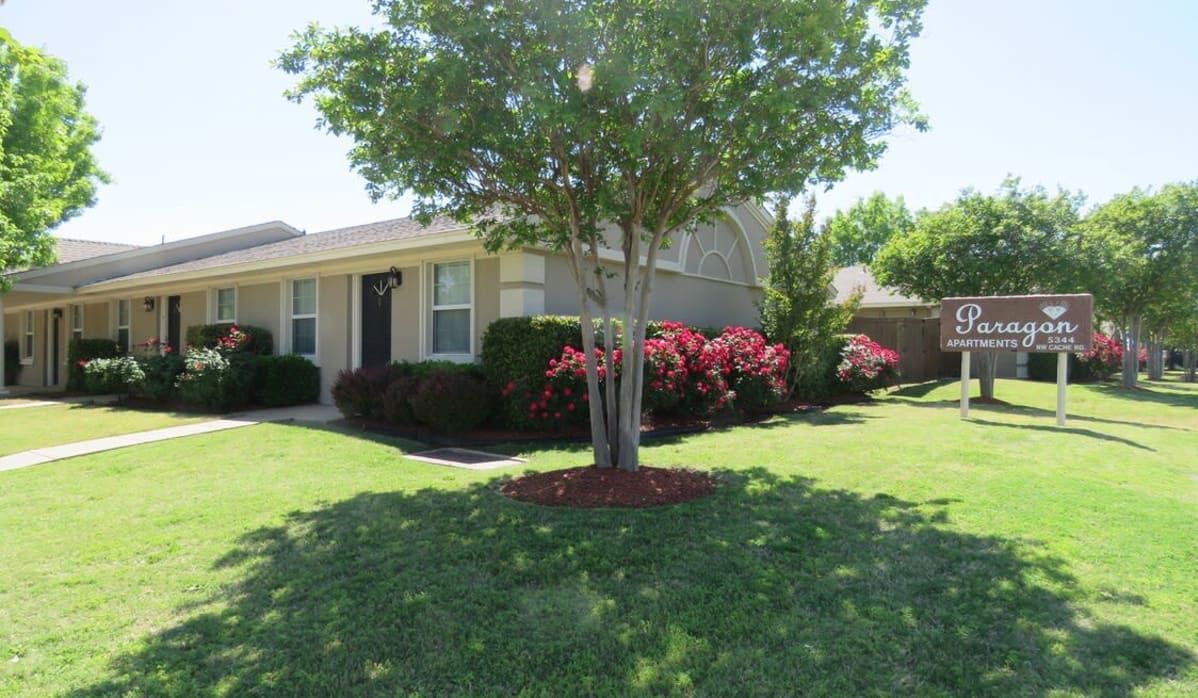 Canyon Apartments exterior on a sunny day with green lawn, trees, red bushes, and a sign.