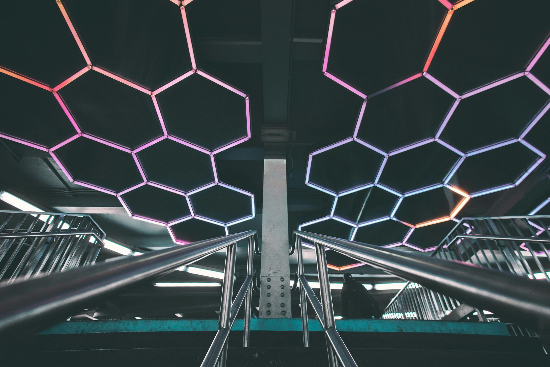 Neon hexagon ceiling lights over a modern escalator corridor with mirrored railings