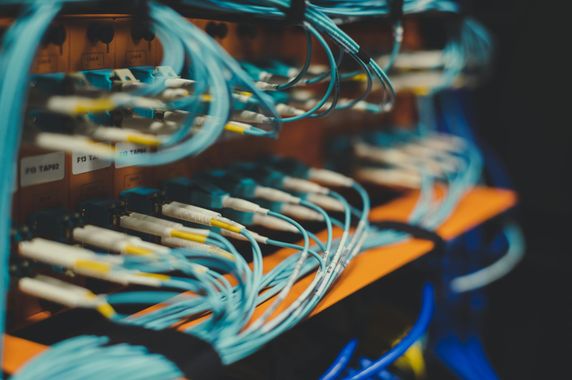 Network cables plugged into a server rack, with blue and orange wires intertwined.