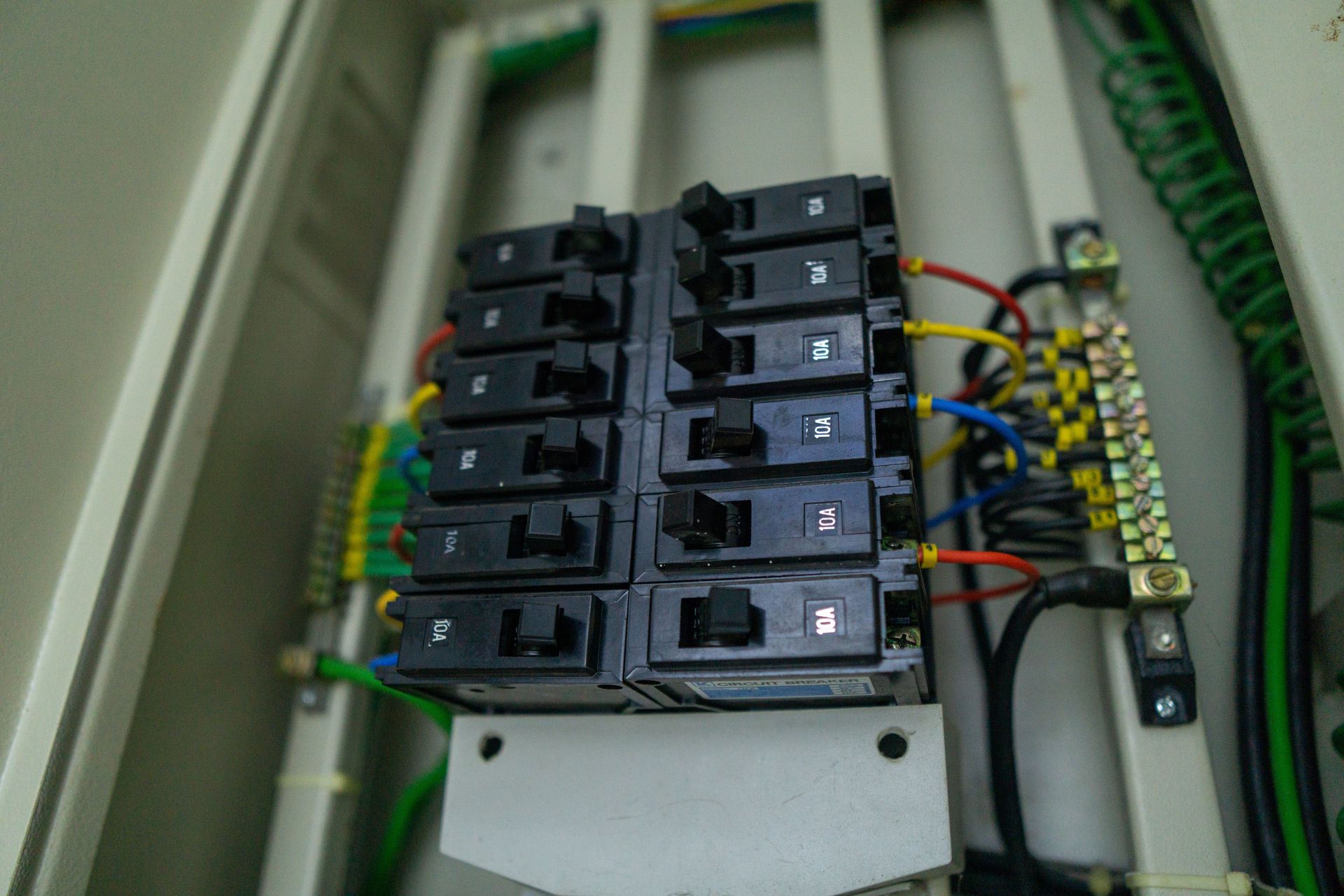 Electrical circuit breaker panel with rows of black switches and colored wires inside a cabinet