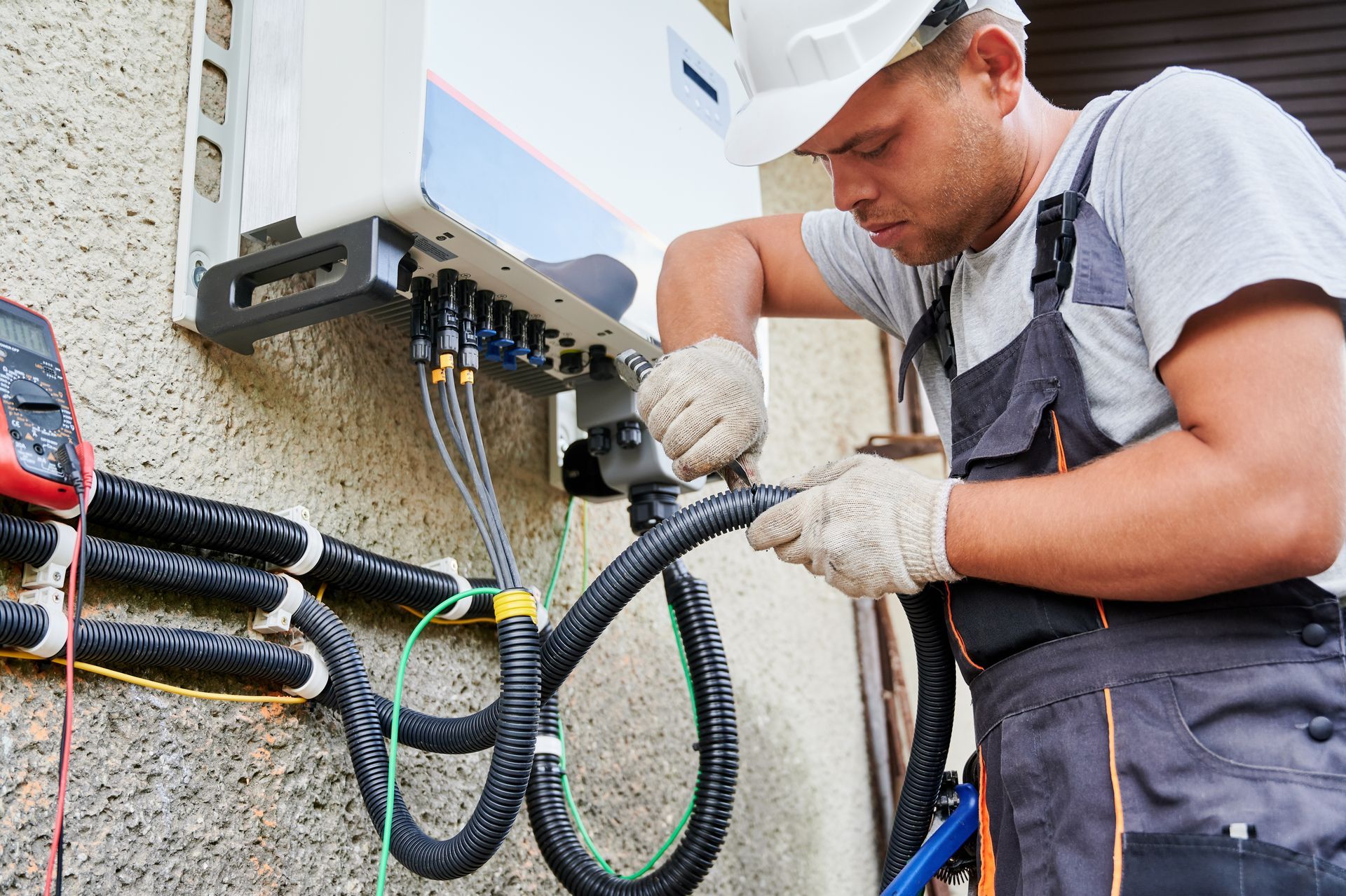 Electrician working on outdoor wall-mounted wiring box with cables and tools
