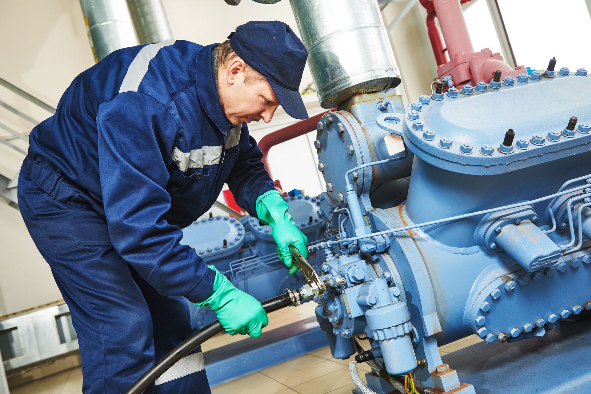 Worker in blue coveralls and gloves inspecting industrial machinery with a wrench
