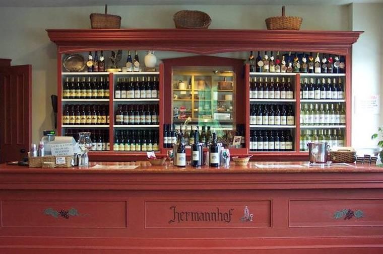 A red wooden bar with shelves filled with numerous wine bottles and three woven baskets on top.