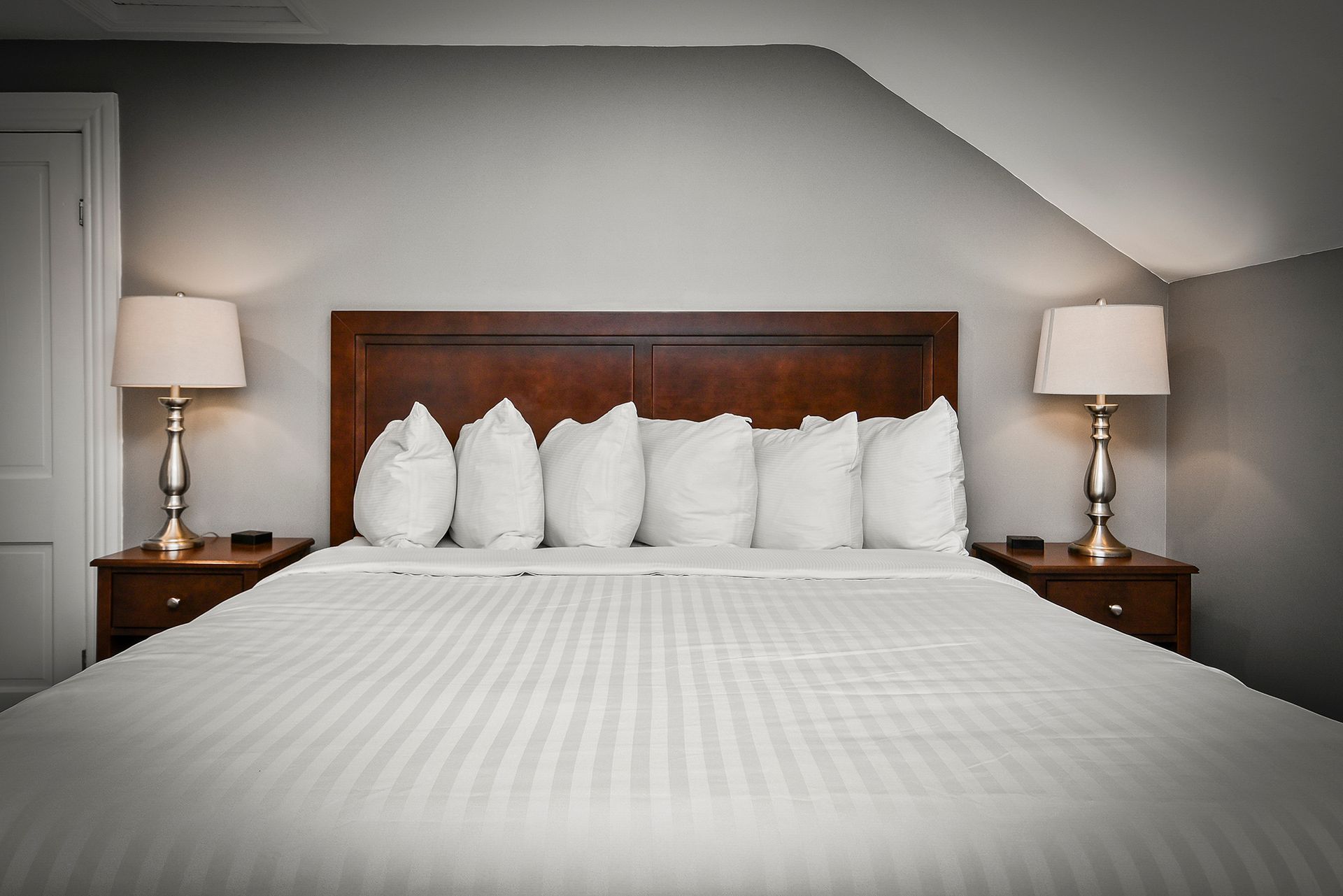 A neatly made bed with white bedding and pillows, featuring a dark wood headboard and lamps on matching nightstands.