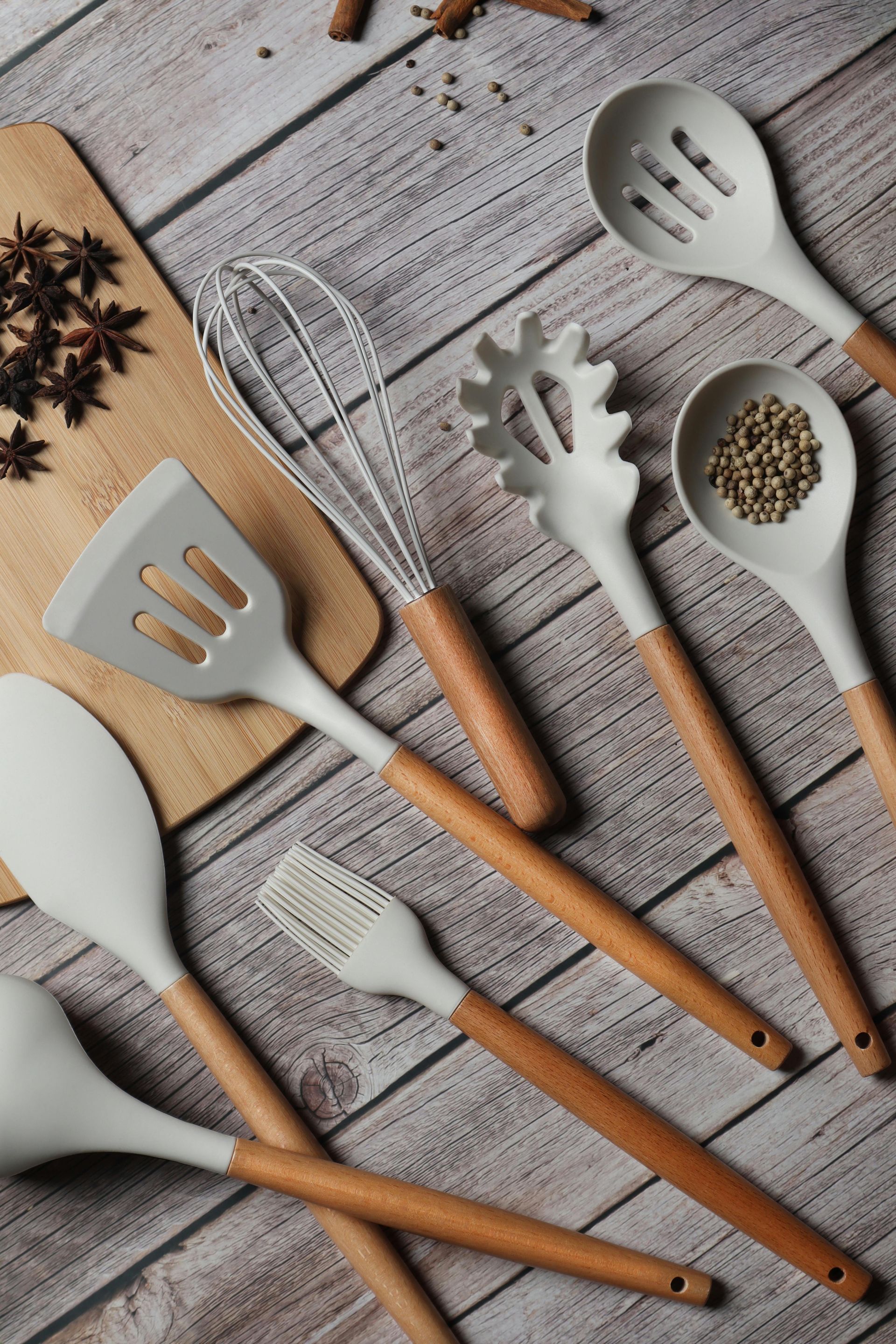 A collection of light-grey silicone kitchen utensils with wooden handles arranged on a rustic wooden table.