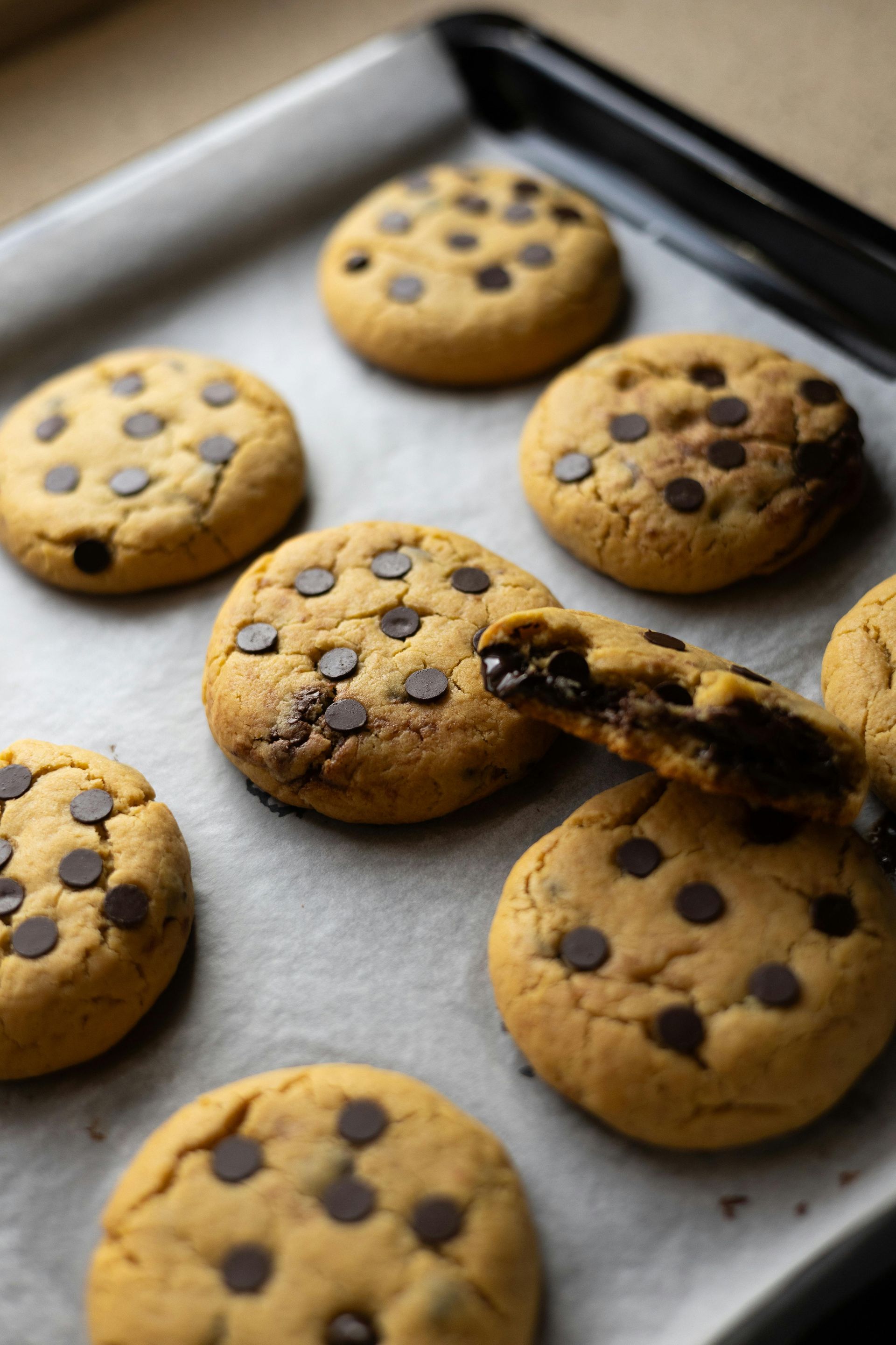 Several freshly baked chocolate chip cookies arranged on a parchment-lined baking sheet.
