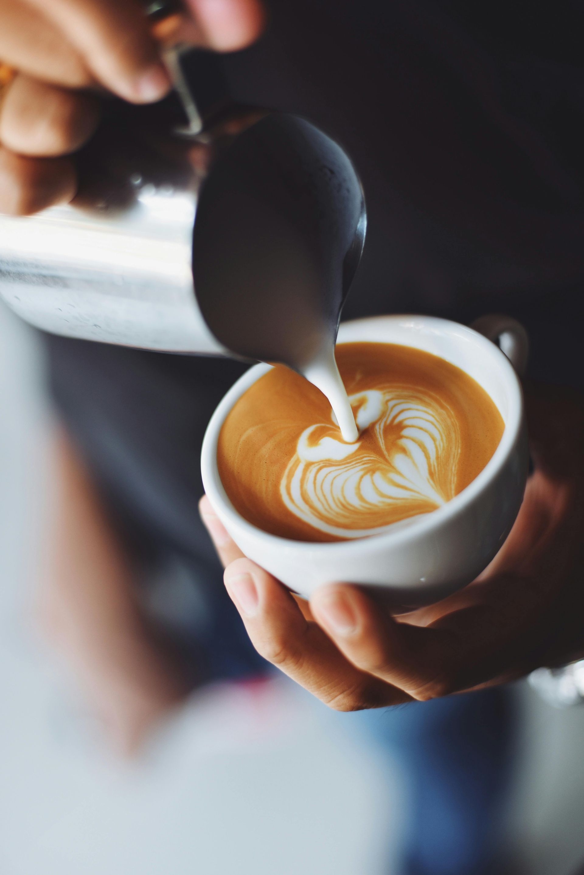 A person pouring steamed milk into a cup of coffee to create heart-shaped latte art.