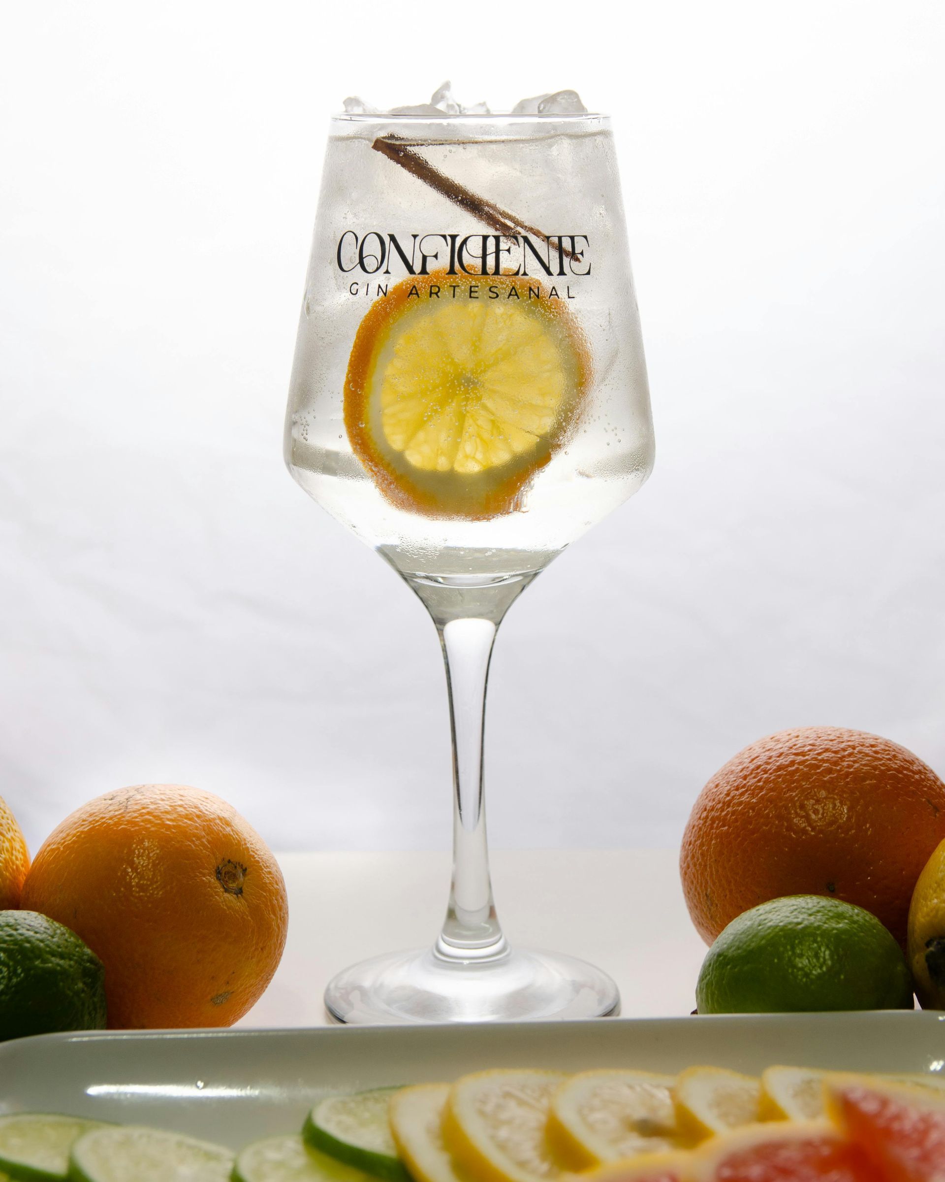 A cocktail in a stemmed glass with an orange slice and cinnamon stick, surrounded by whole and sliced citrus fruits.