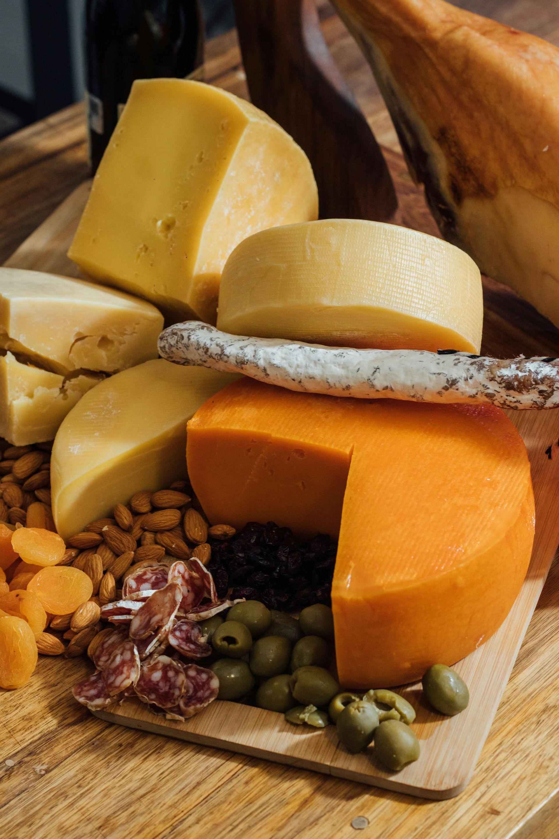 A charcuterie board featuring various cheeses, dried fruits, almonds, cured sausage, and olives on a wooden table.