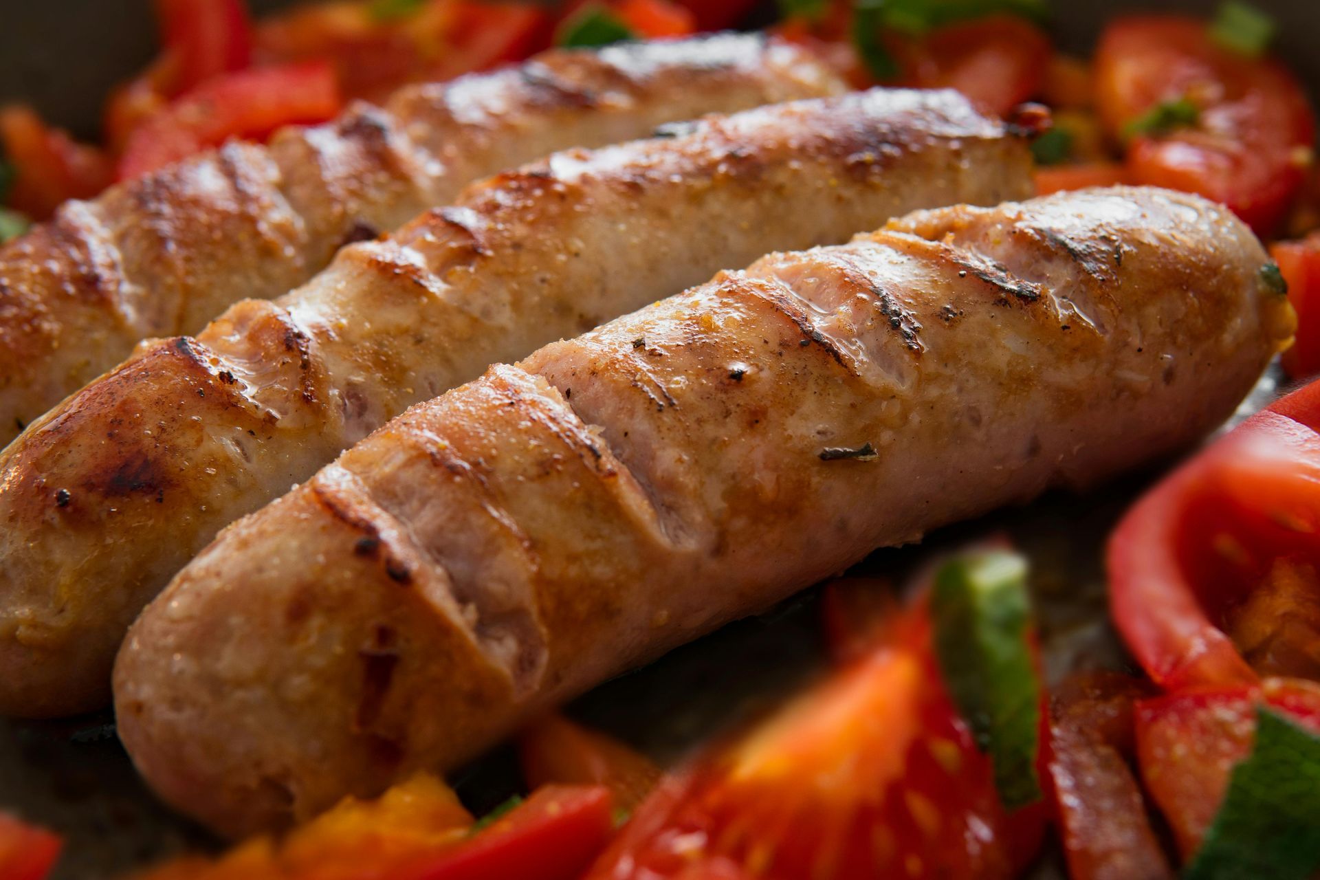 Three grilled sausages resting on a bed of fresh, diced tomatoes and herbs.