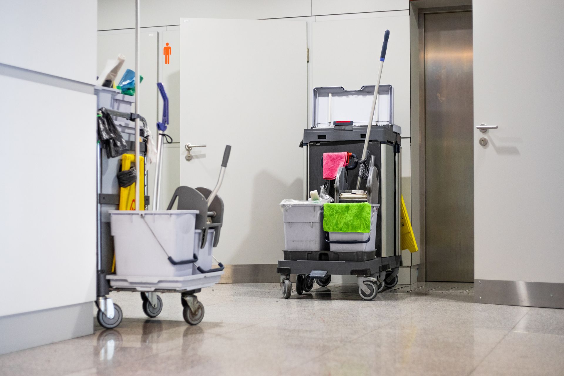 A cleaning cart with tools, cleaning buckets, and cleaning equipment standing in a corridor