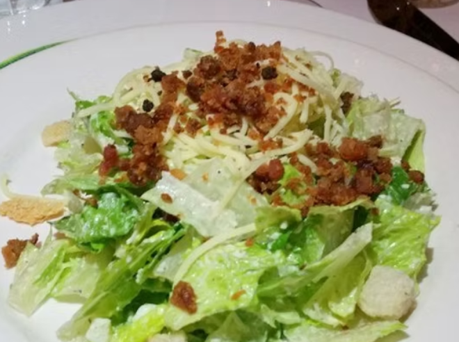 Caesar salad on a white plate with romaine lettuce, parmesan cheese, croutons, and bacon bits.