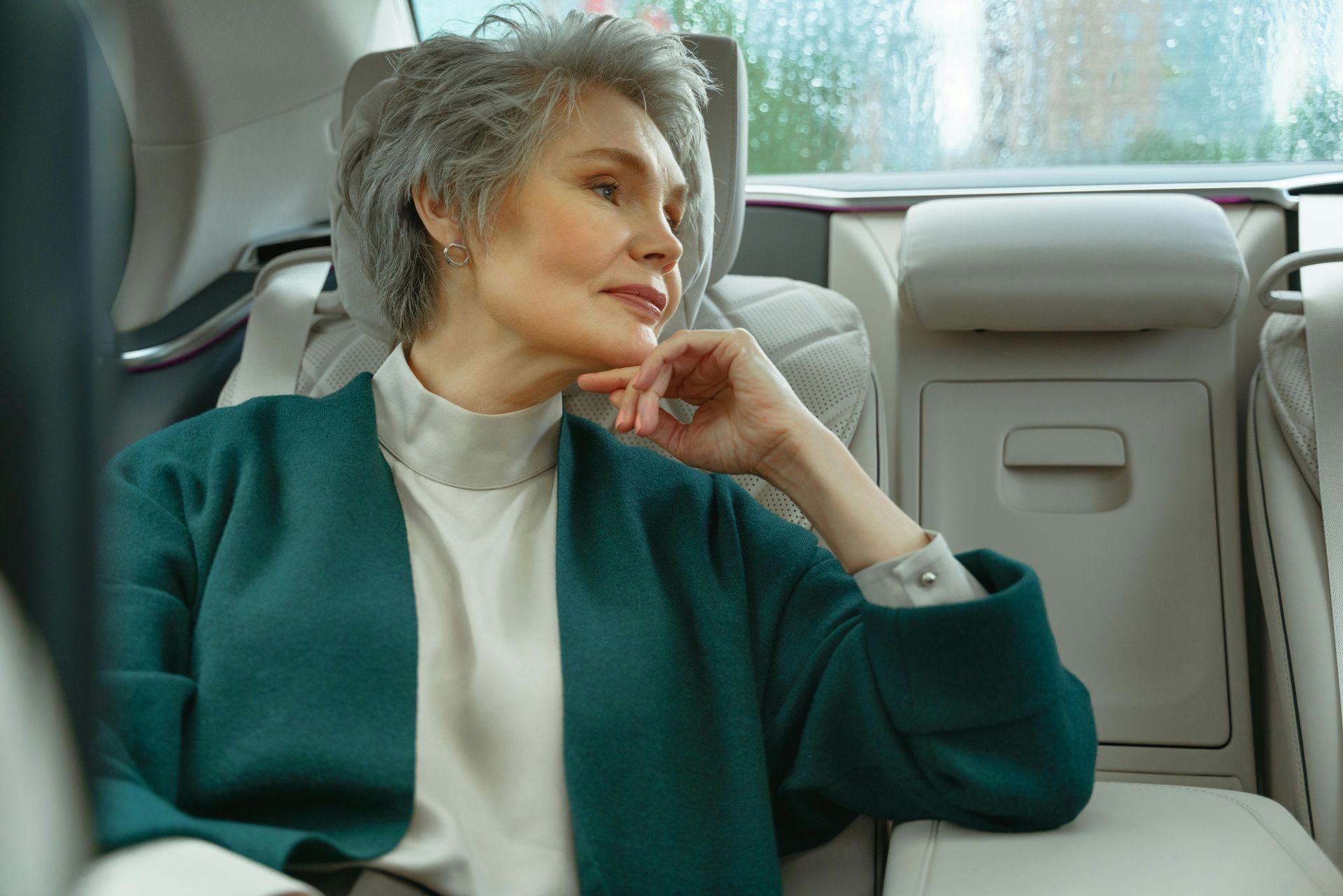 Older woman with gray hair in a car, looking out the window. She wears a green cardigan and white top.