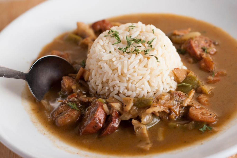 Gumbo with sausage, vegetables, and a scoop of white rice on a white plate.