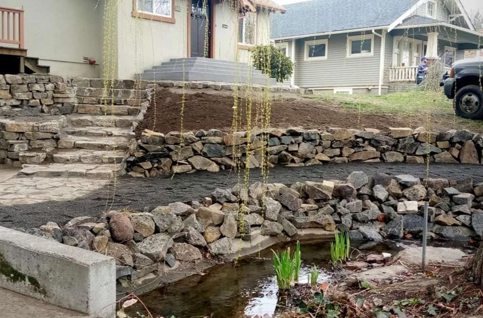 Stone steps and retaining walls in front yard with small pond and weeping willow.