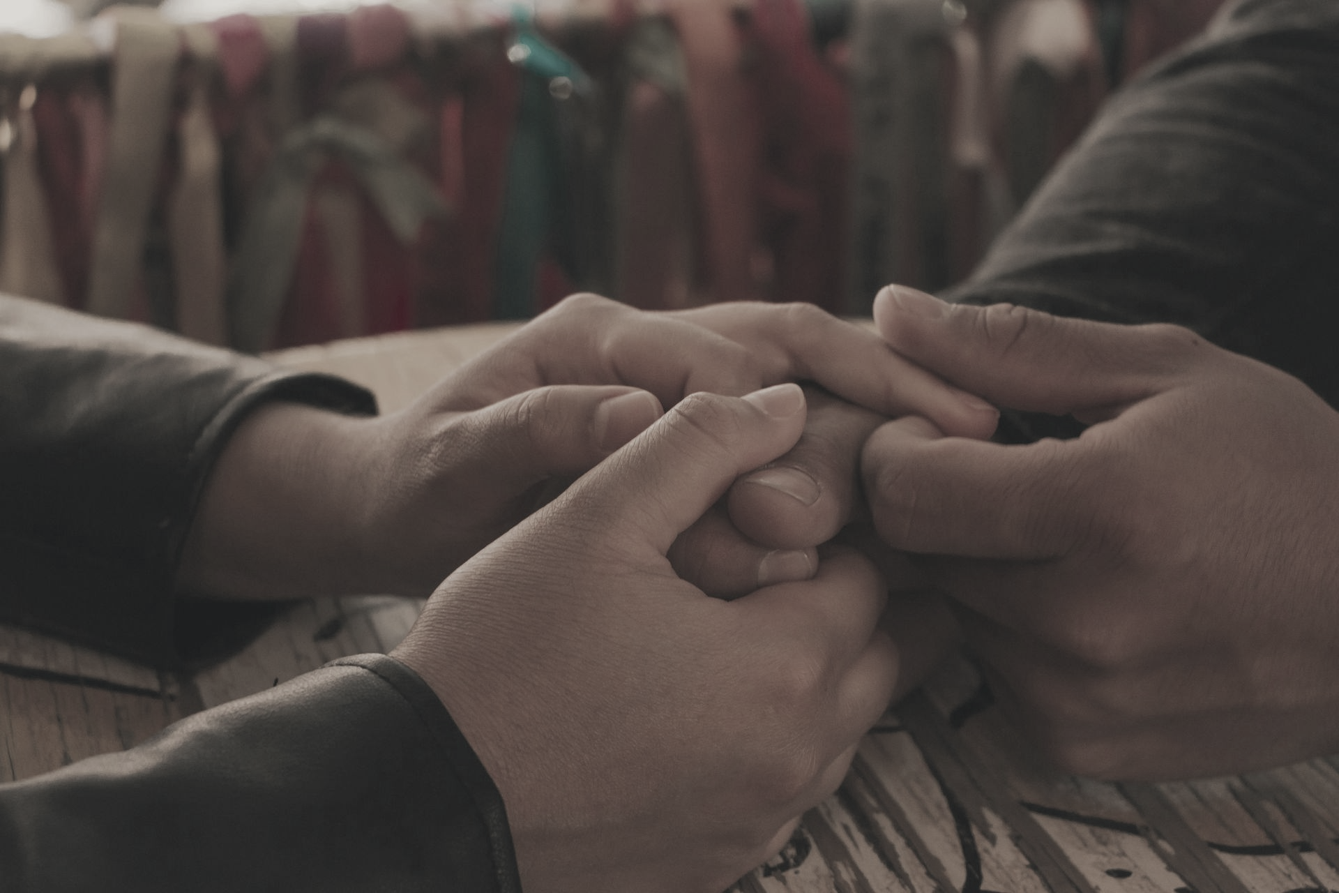 Two people holding hands across a wooden table, suggesting a moment of support or connection.