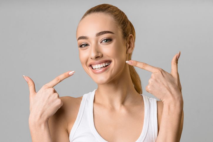 A woman is pointing at her teeth and smiling.