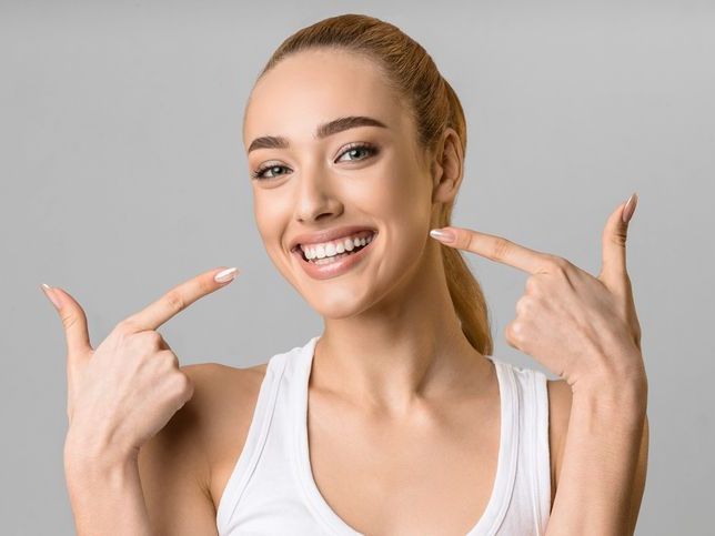 A woman is smiling and pointing at her teeth.