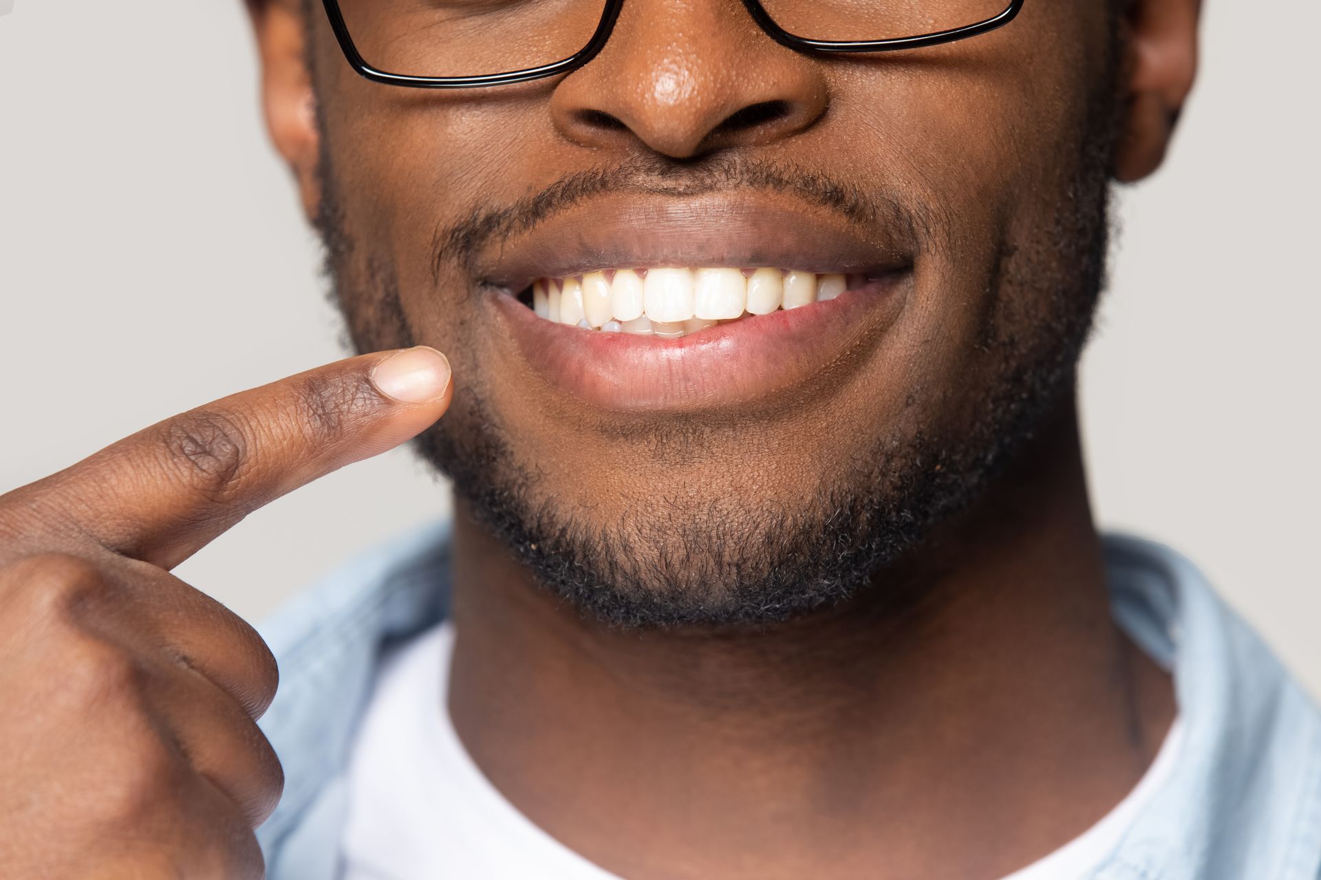 A close up of a man wearing glasses pointing at his teeth.