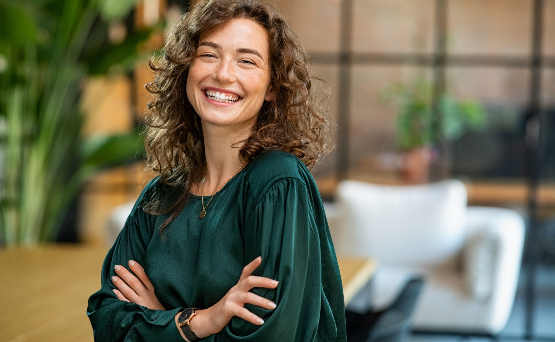 A woman in a green shirt is smiling with her arms crossed.