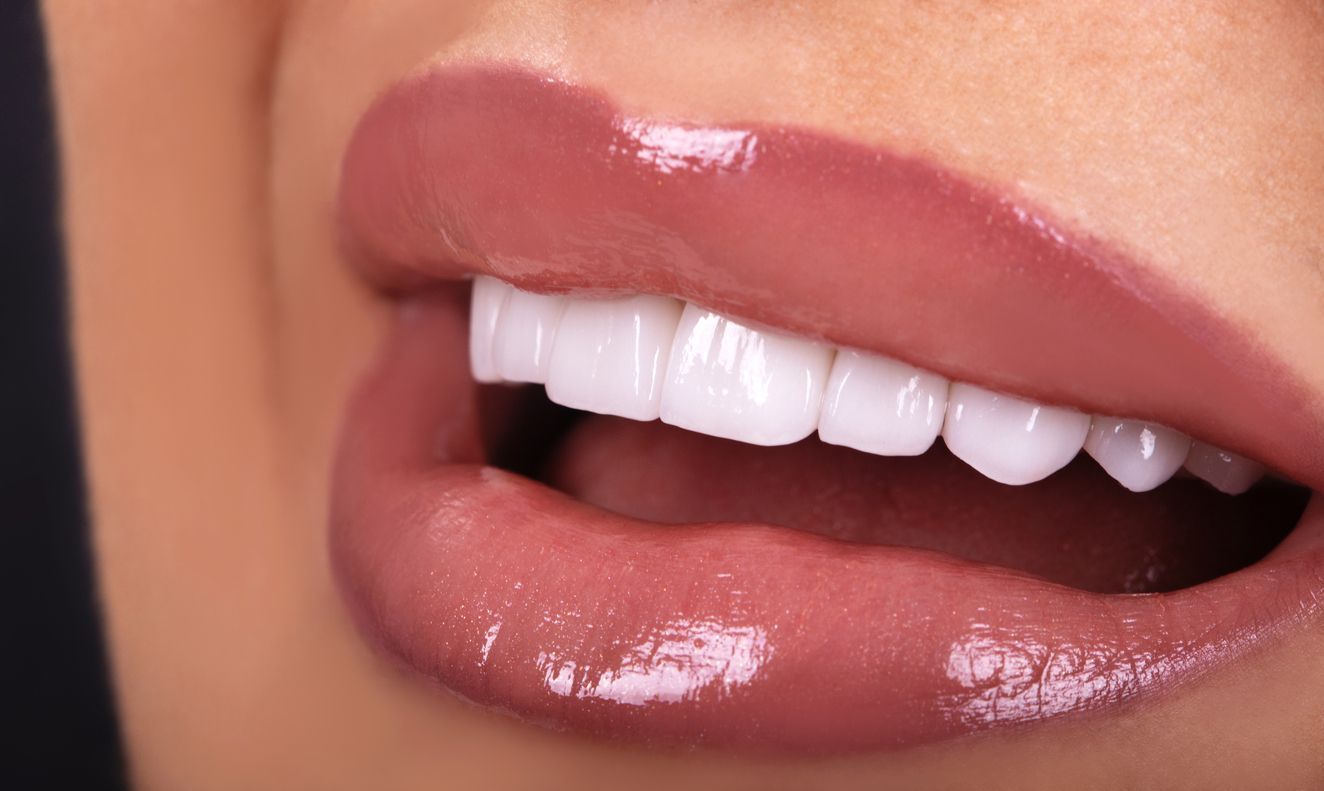 A close up of a woman 's mouth with white teeth and pink lips.