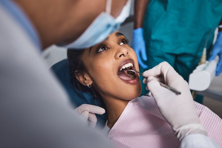 A woman wearing sunglasses is getting her teeth examined by a dentist.