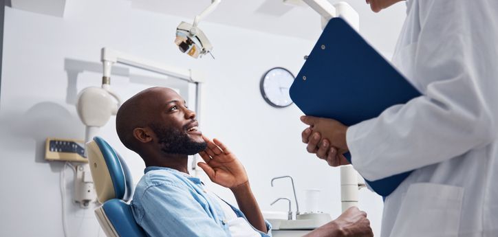 A man is sitting in a dental chair talking to a dentist.