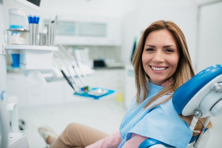 A woman is smiling while sitting in a dental chair.